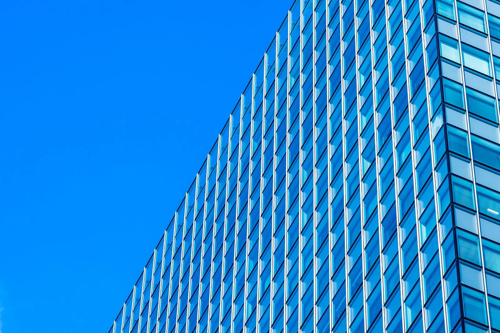 A blue glass tower photographed from the street, reaching into clear sky